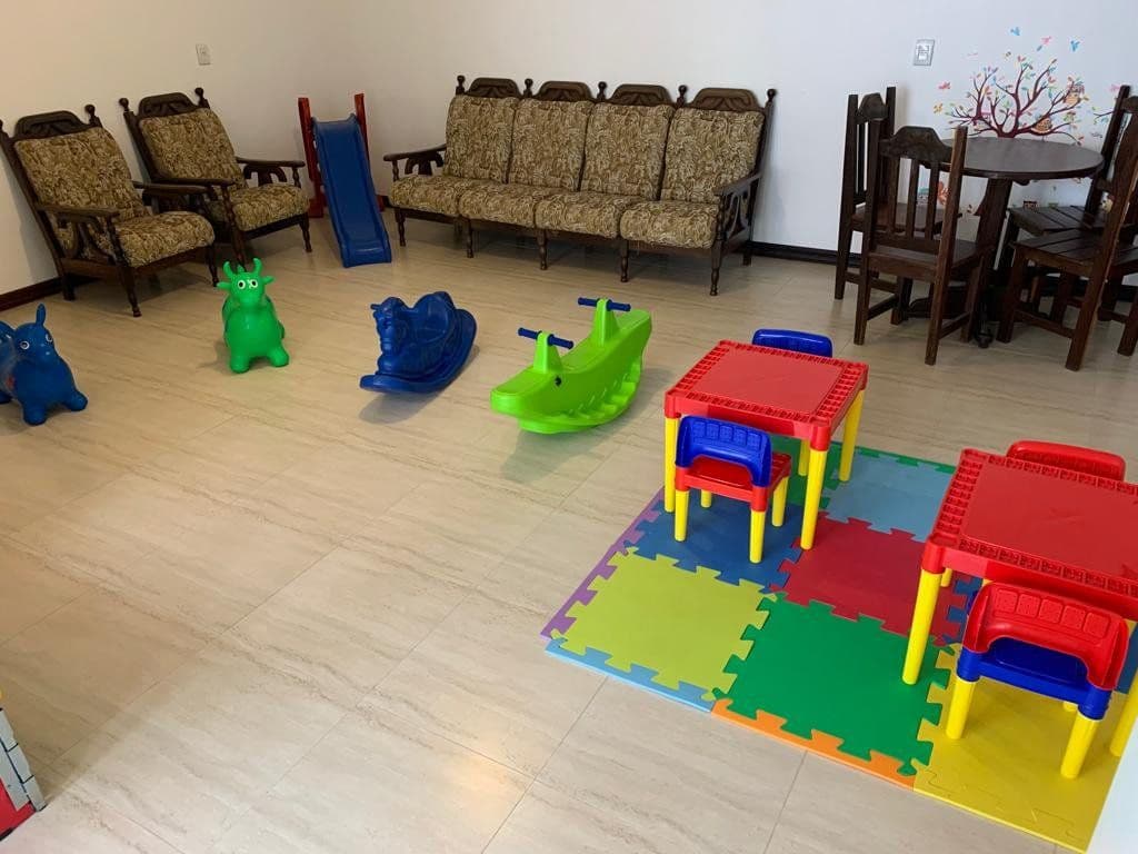 Espaço kids com gangorras, mesinhas e tapete colorido